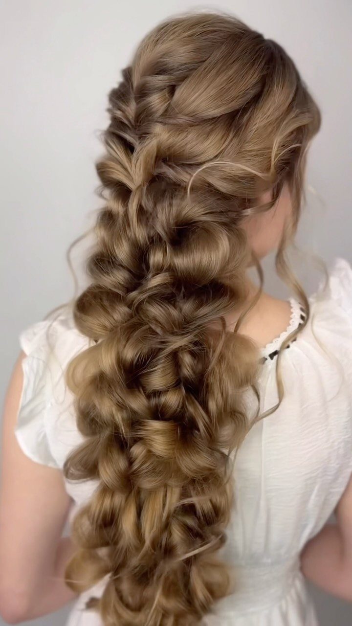 Long light brown hair styled in a thick, voluminous, loose braided ponytail.