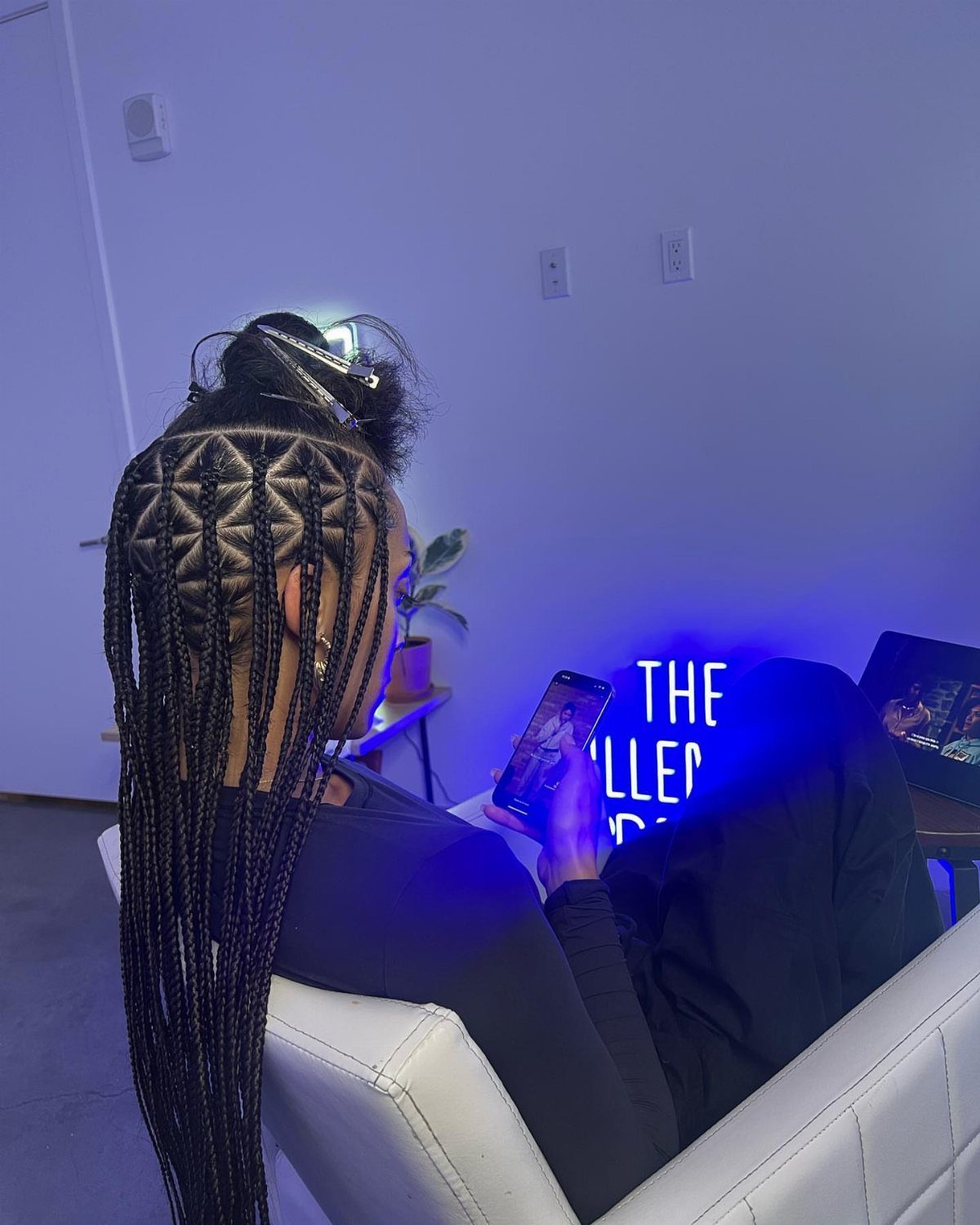 Woman with triangle box braids sitting in a chair using her smartphone.