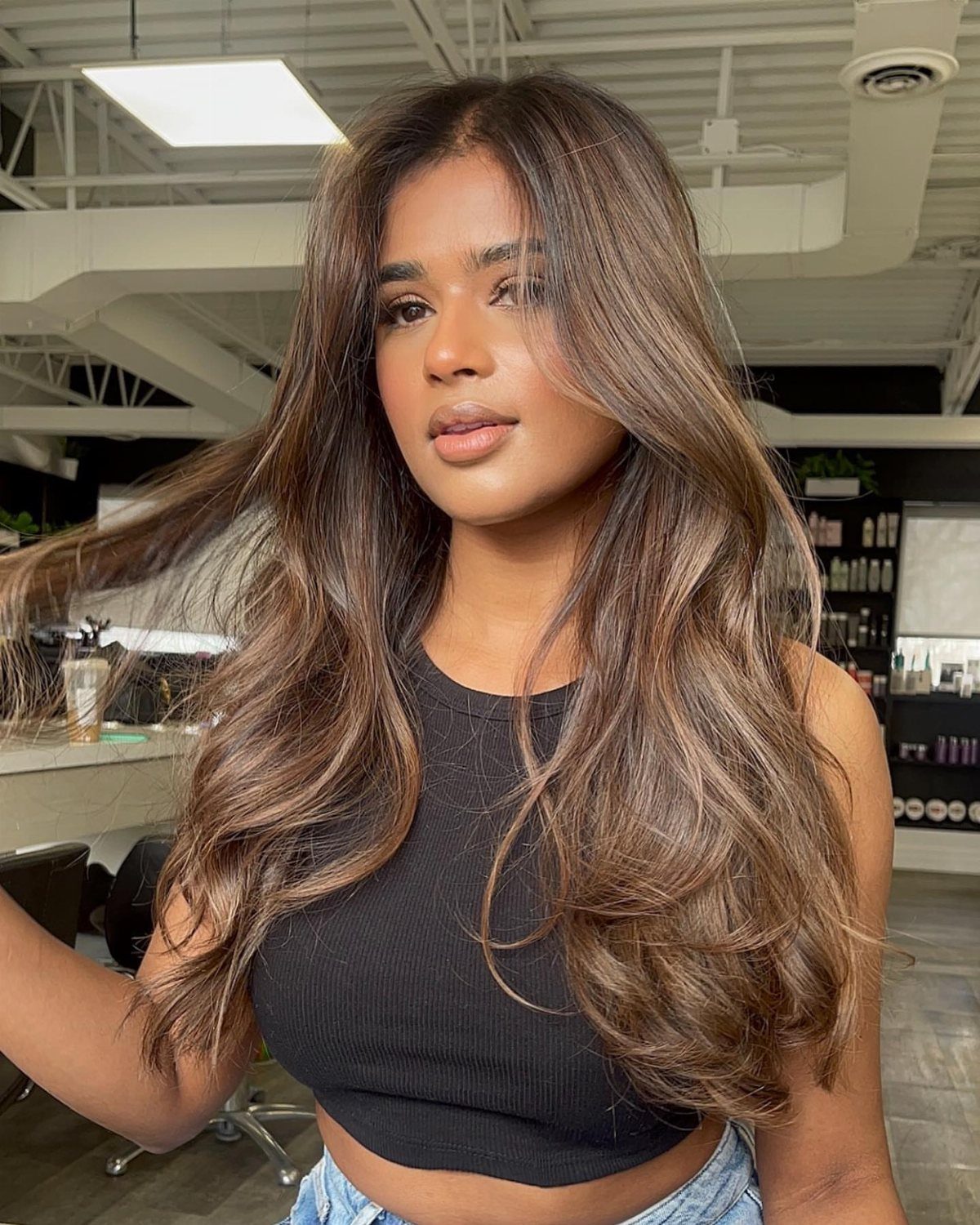 14 Different Color Hair Ideas for Every Skin Tone 8 Woman with long wavy brown hair and blended highlights in a hair salon