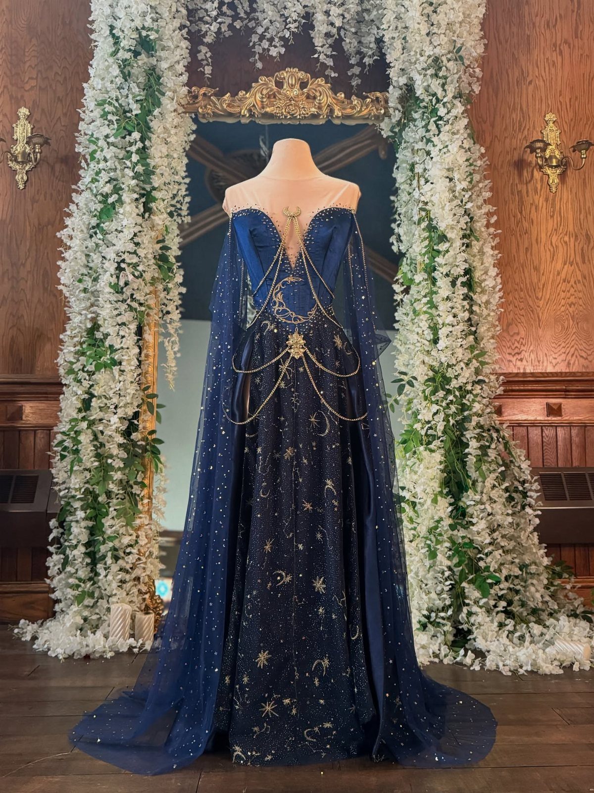 Dark blue celestial gown with gold stars and a sheer cape on a mannequin