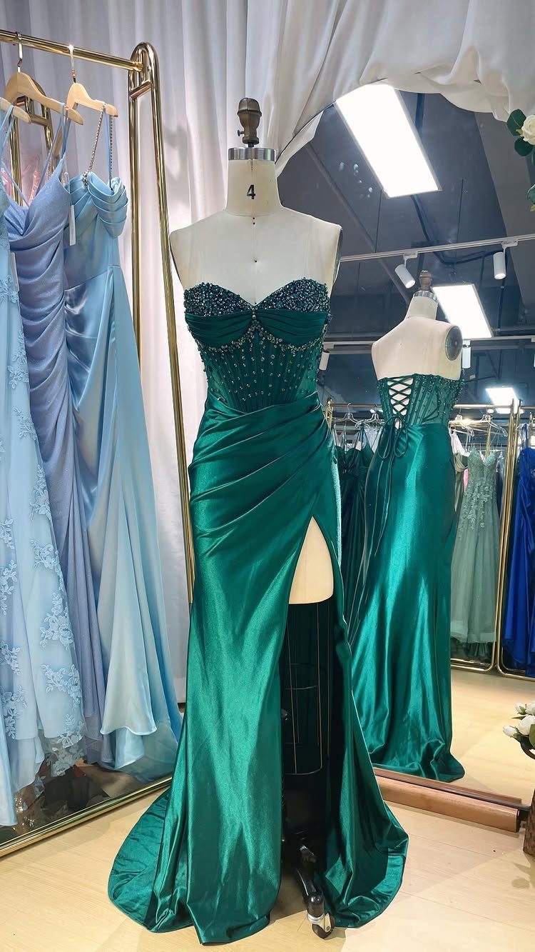 Emerald green satin prom dress with a beaded corset bodice on a mannequin.