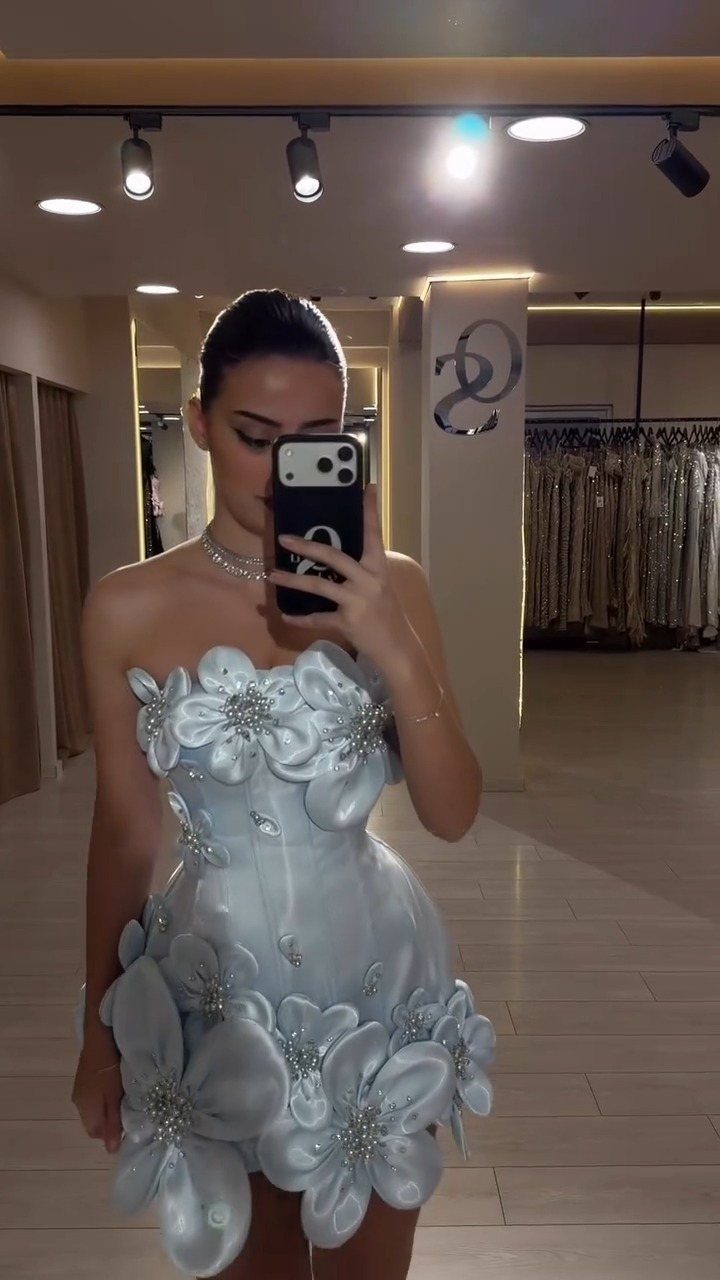Woman in a light blue strapless mini dress with large 3D floral details.