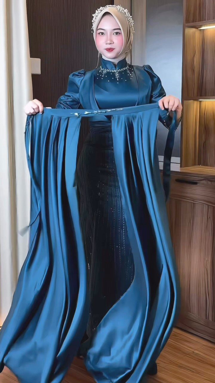 Woman in teal satin gown holding up a matching detachable overskirt