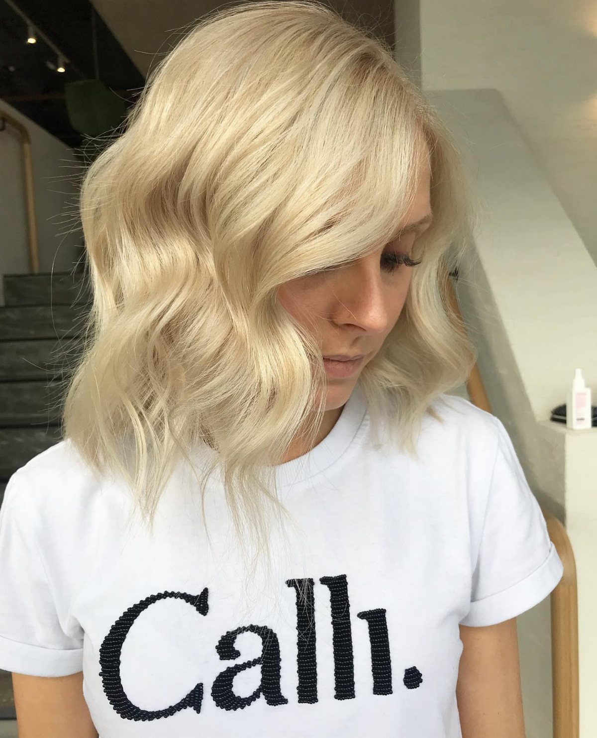Fall Hairstyles and Color: 16 Ideas, Caramel to Espresso 16 Woman with wavy creamy blonde hair wearing a white graphic t-shirt.