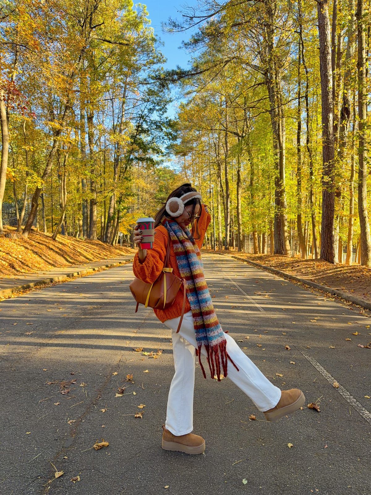 Fall Orange Outfits: 10 Ideas for Every Occasion 2 Person in orange cardigan and white trousers posing on a road with autumn trees.