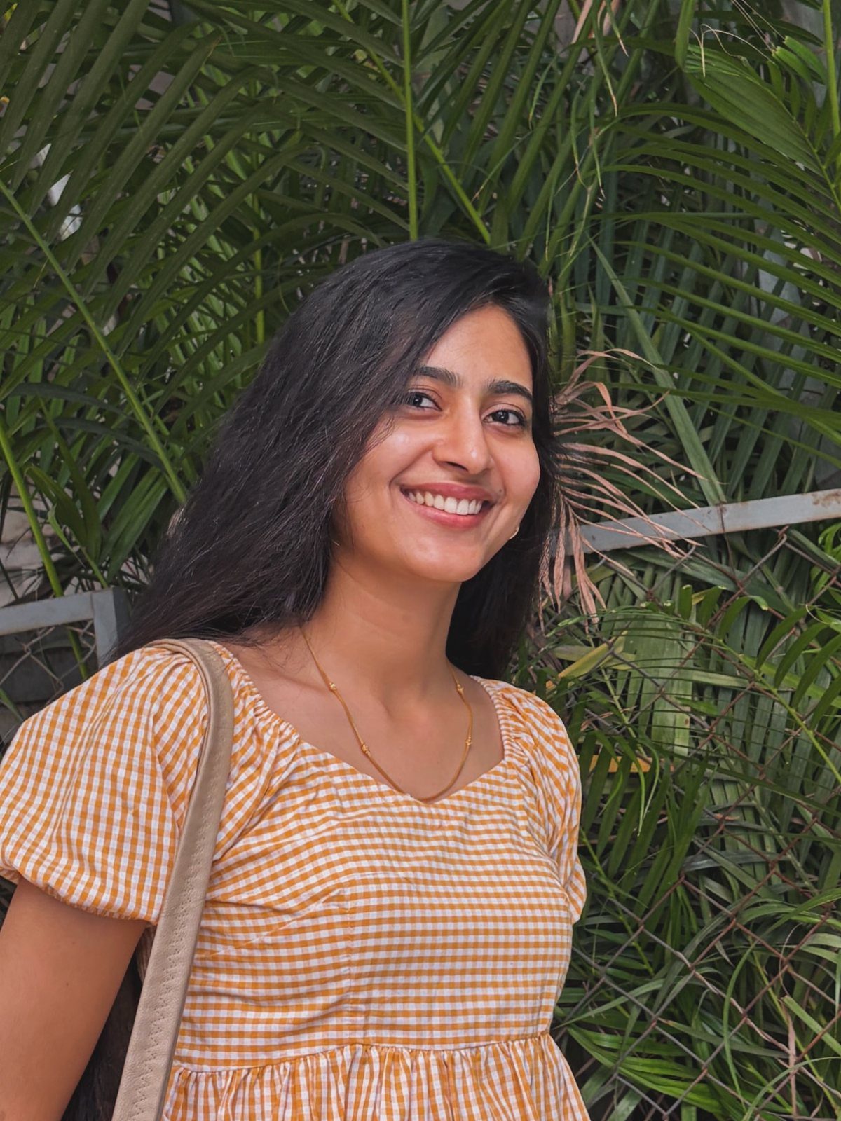 Fall Orange Outfits: 10 Ideas for Every Occasion 3 Woman smiling wearing an orange and white gingham top against green palm leaves