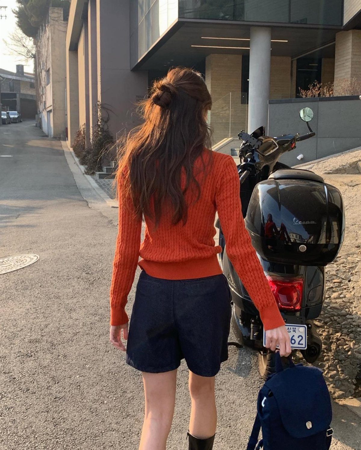 Fall Orange Outfits: 10 Ideas for Every Occasion 10 Woman from behind wearing an orange ribbed sweater and dark blue shorts.