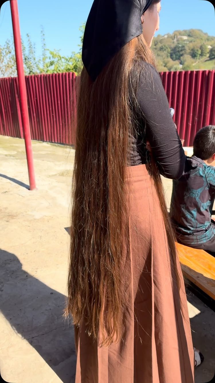 Woman with brown floor length hair wearing a headscarf and long brown skirt.