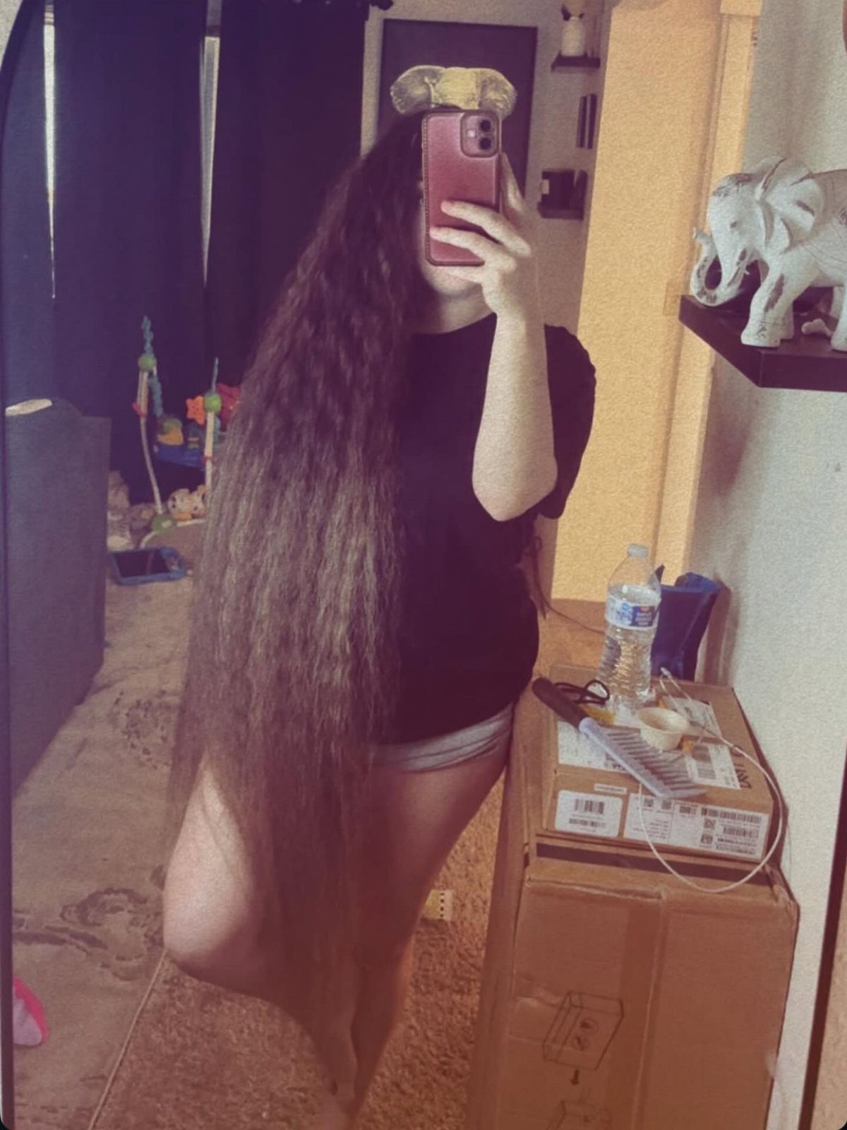 Person with floor length brown wavy hair taking a mirror selfie in a room