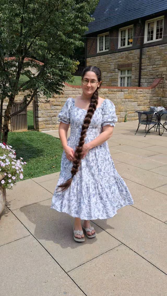 Woman with a floor-length dark brown braid wearing a floral dress on a patio