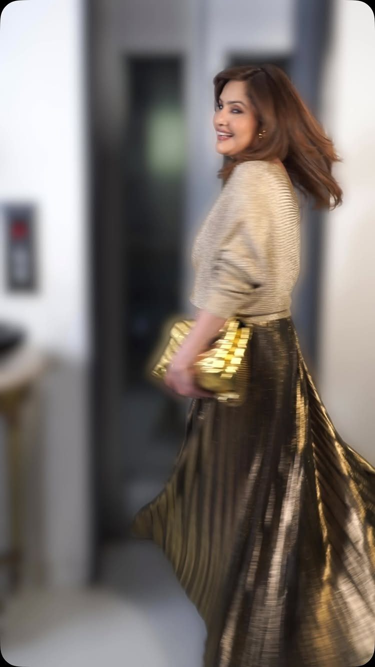 Woman wearing a gold pleated maxi skirt and matching top with gold clutch