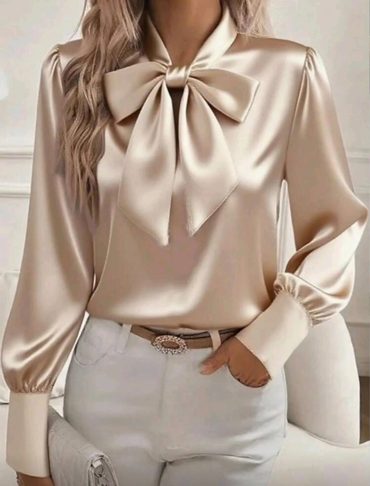 Champagne gold satin blouse with a bow tie paired with white trousers.