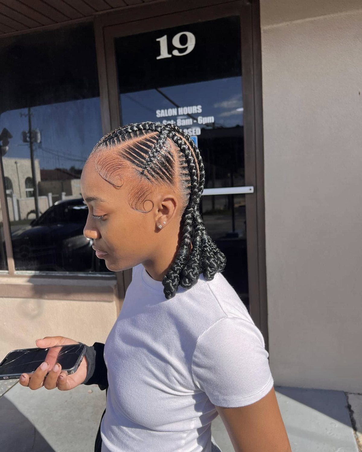 Woman with black hair styled in criss-cross cornrows gathered into a ponytail.