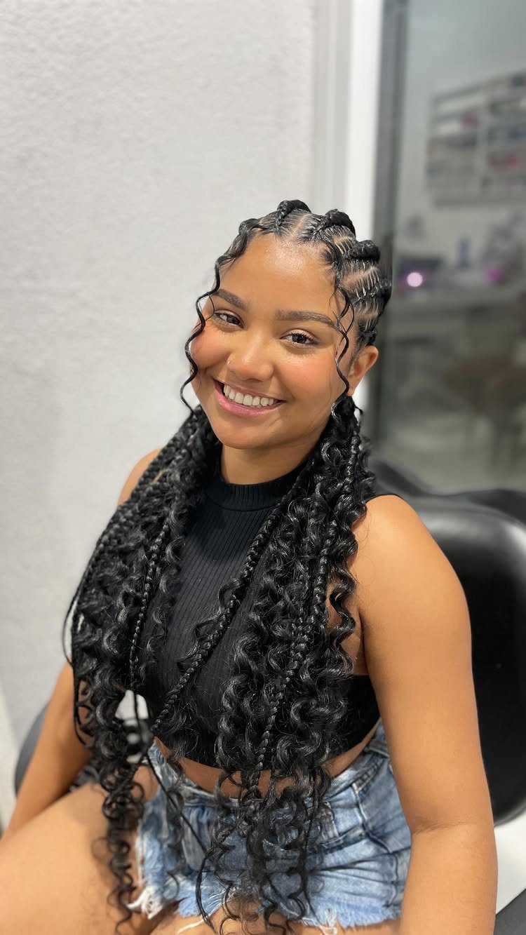 Woman with black Ghana braids and curly ends smiling in a room.