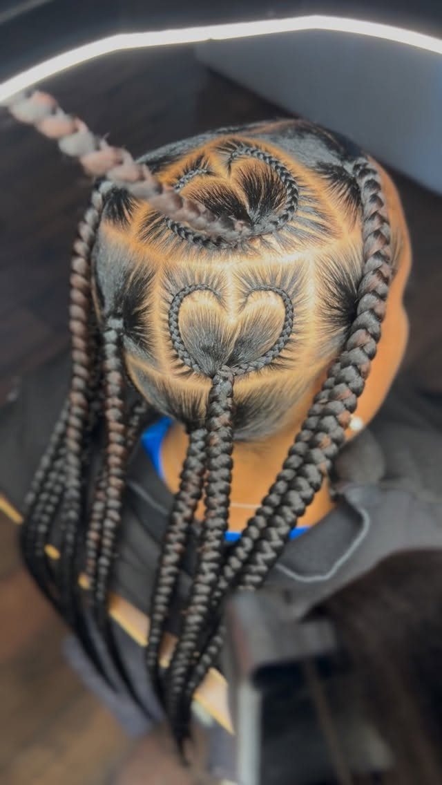 Thick black braids with heart-shaped patterns braided into the scalp and blonde highlights.