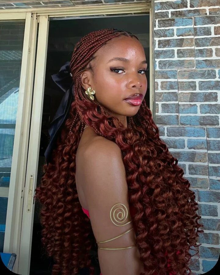 Woman with reddish-brown hair featuring small braids transitioning into long, flowing curly ends.