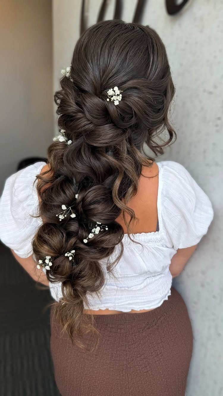Long brown hair styled in a loose pull-through braid with white baby's breath flowers.