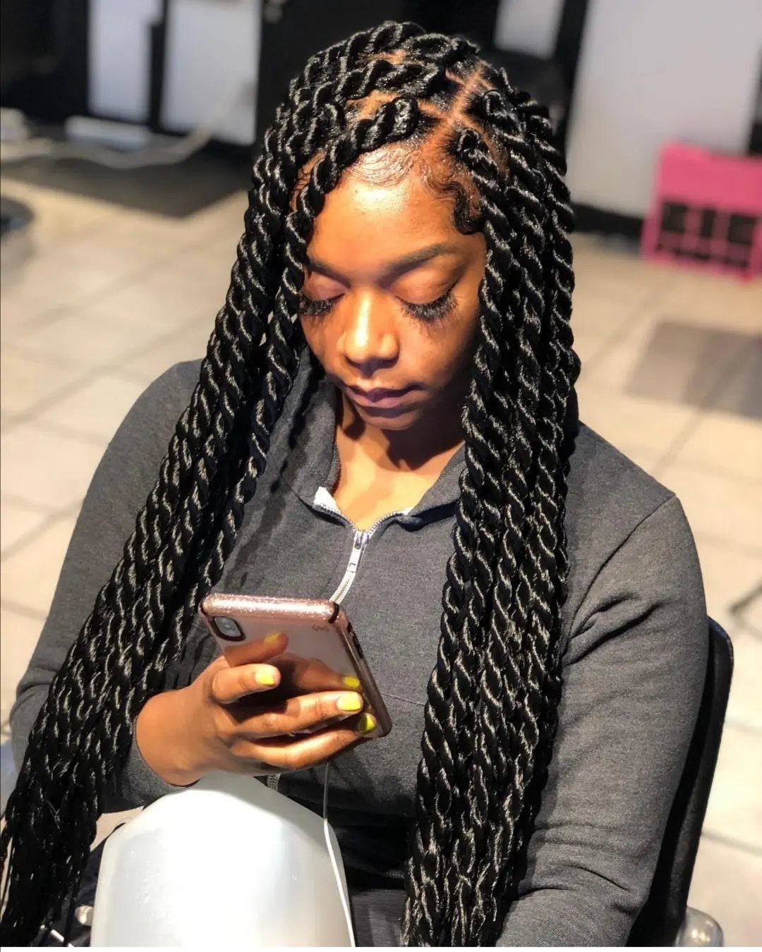Woman with long black rope twist braids looking at her gold smartphone.