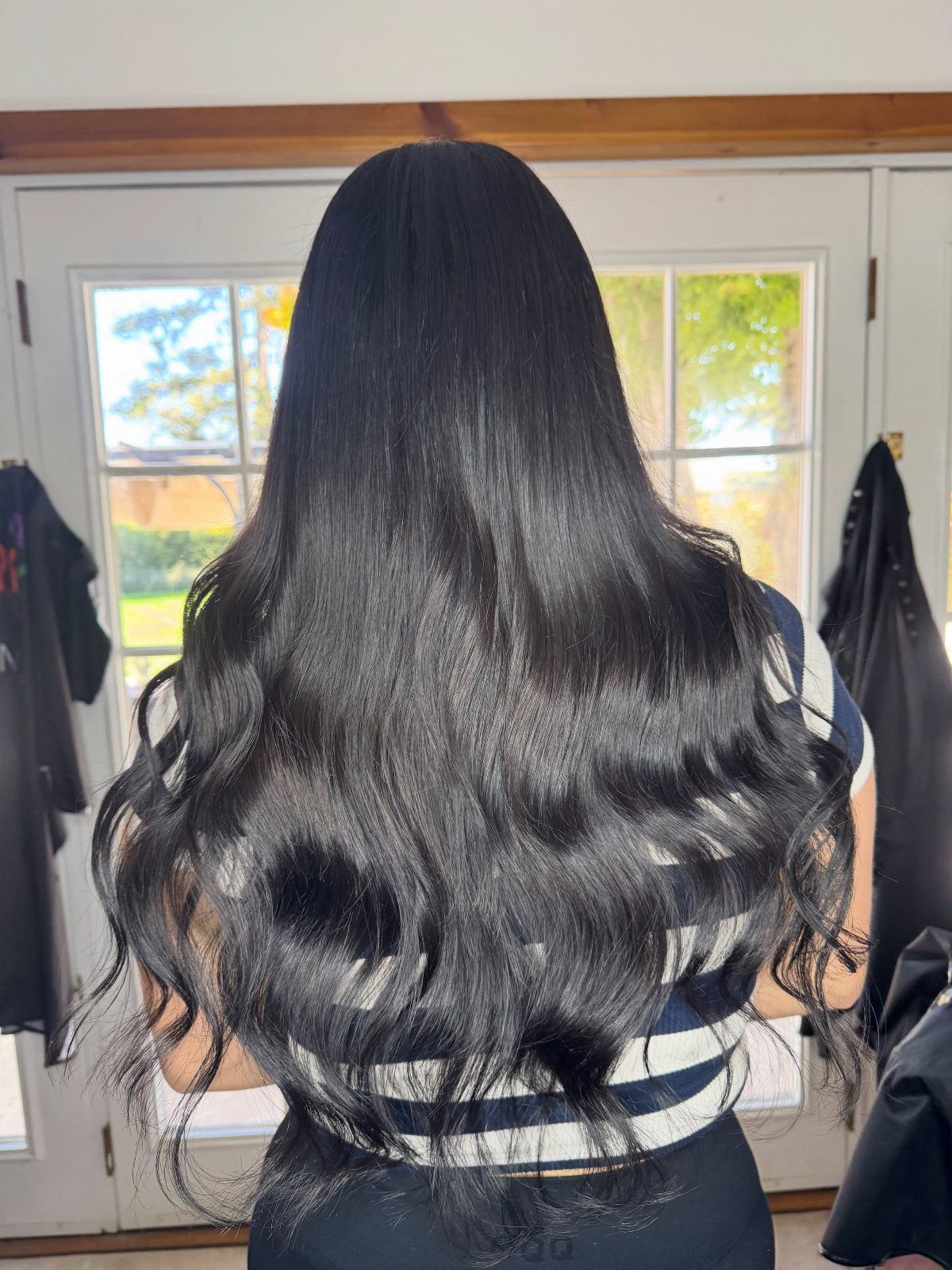 Long, shiny black wavy hair seen from behind against a white door background.