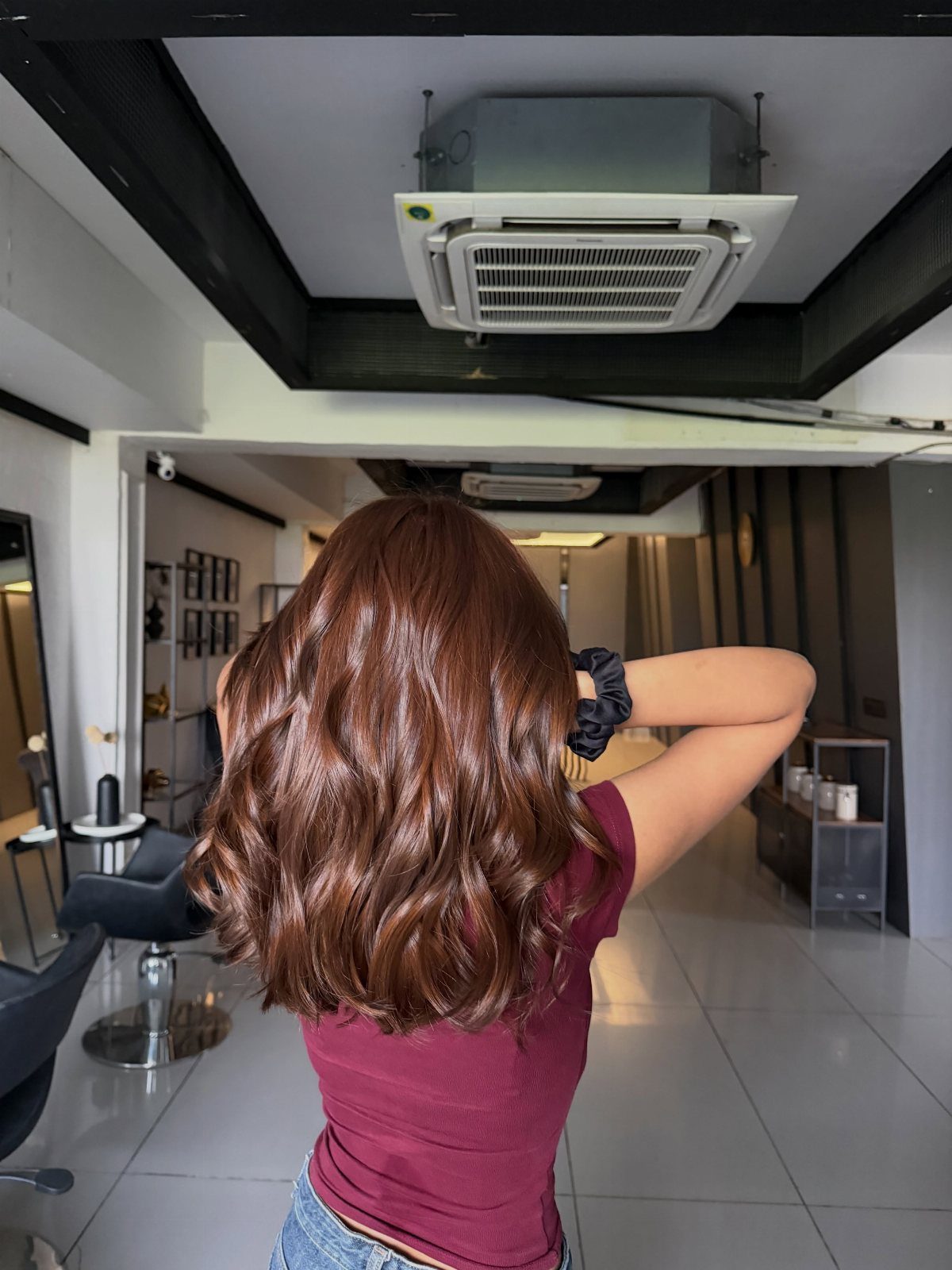 Woman with shiny, wavy reddish-brown hair posing in a modern hair salon.