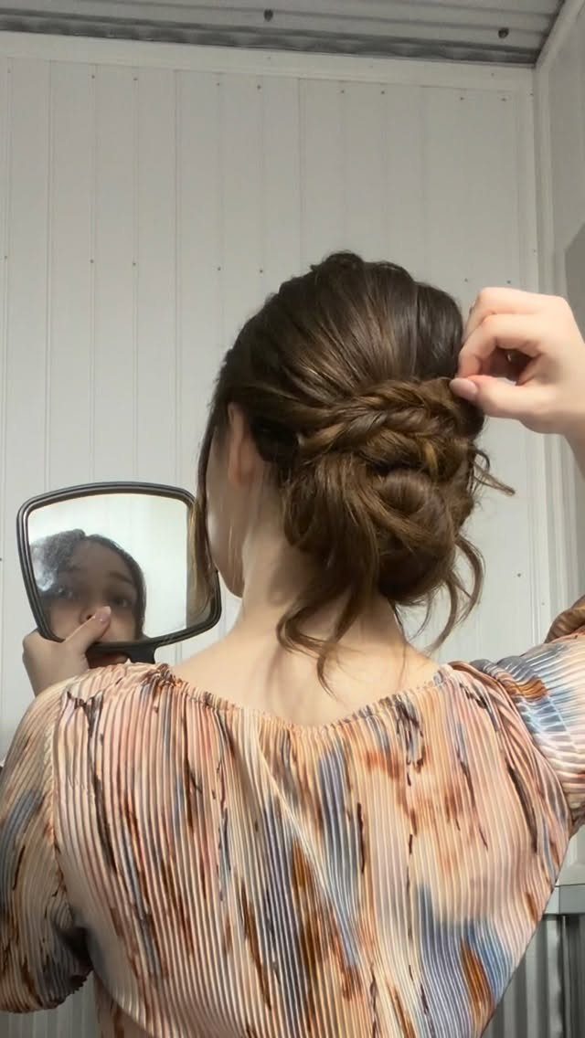 Woman with brown hair in a braided updo looking into a hand mirror