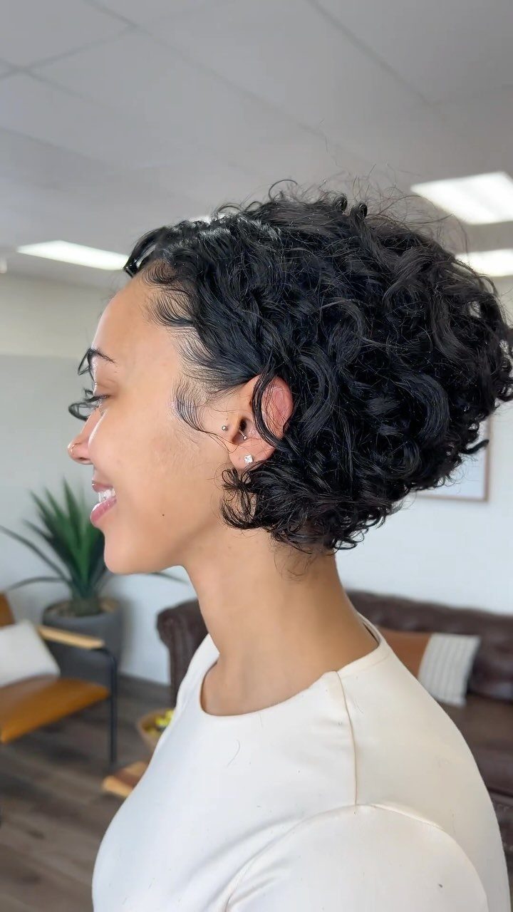 Woman with a chin-length curly bob hairstyle in a bright indoor setting.