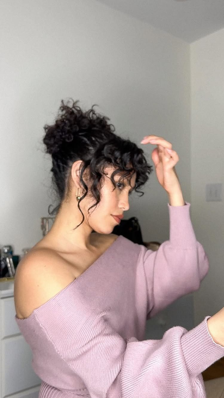 Woman with dark curly hair featuring curly bangs and a high updo.