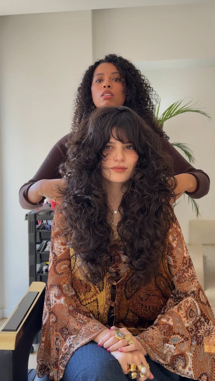 Woman with a curly shag haircut and bangs sitting in a salon chair.