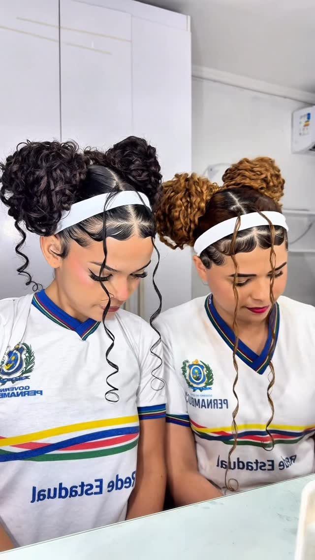 Woman with curly hair styled in double buns and a white headband.