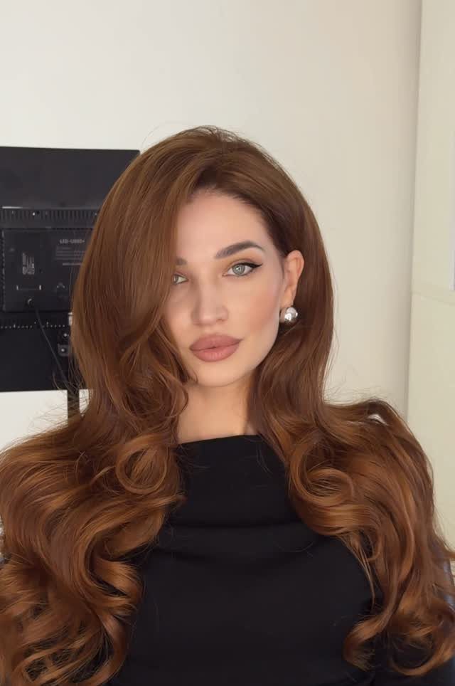 Woman with voluminous auburn hair styled in a bouncy blowout with large curls.