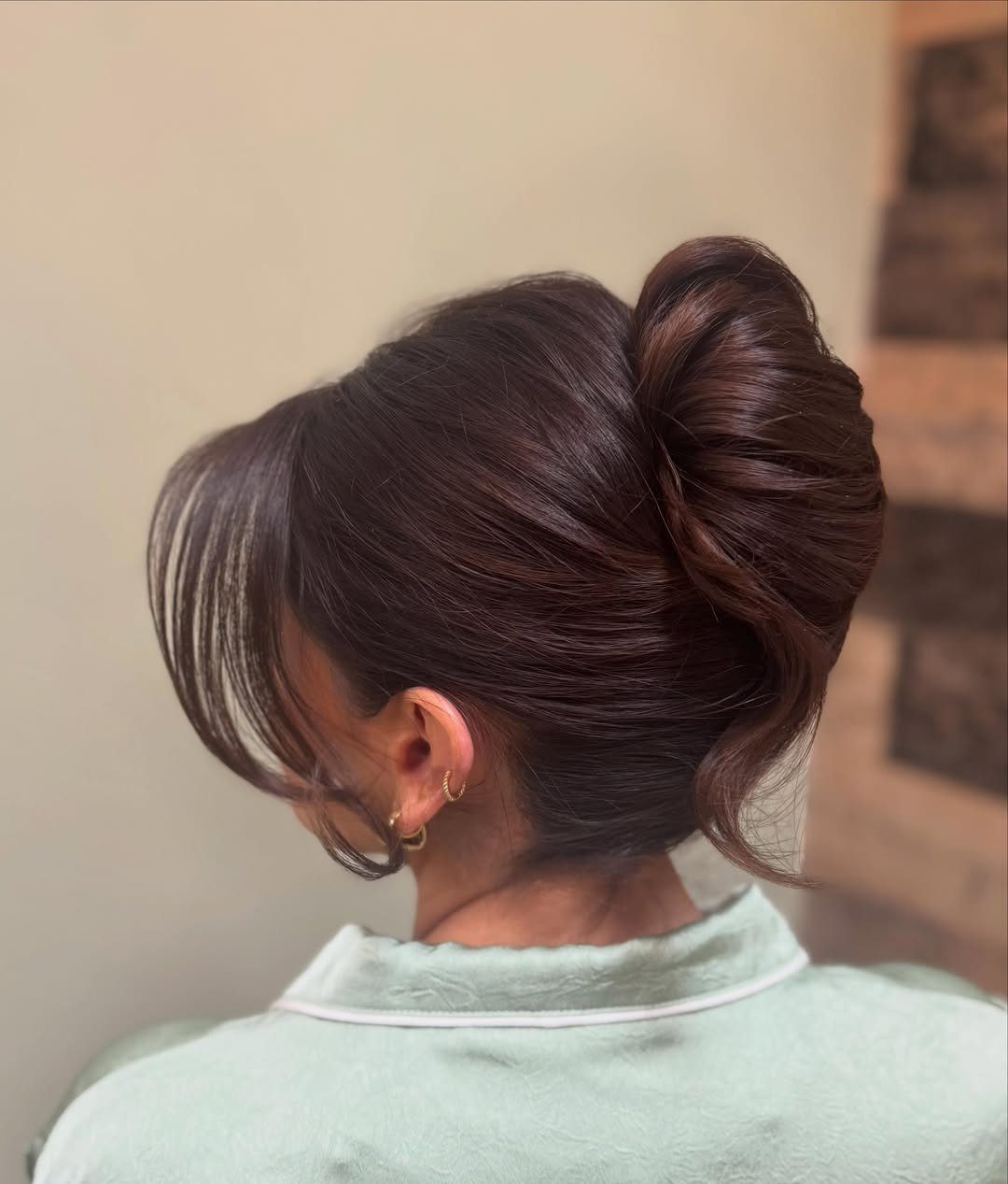 Woman with dark brown hair styled in a high, elegant sculpted bun.