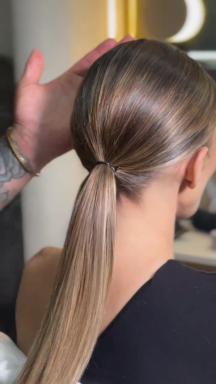 Sleek low ponytail on brown hair being adjusted by a stylist's hand.