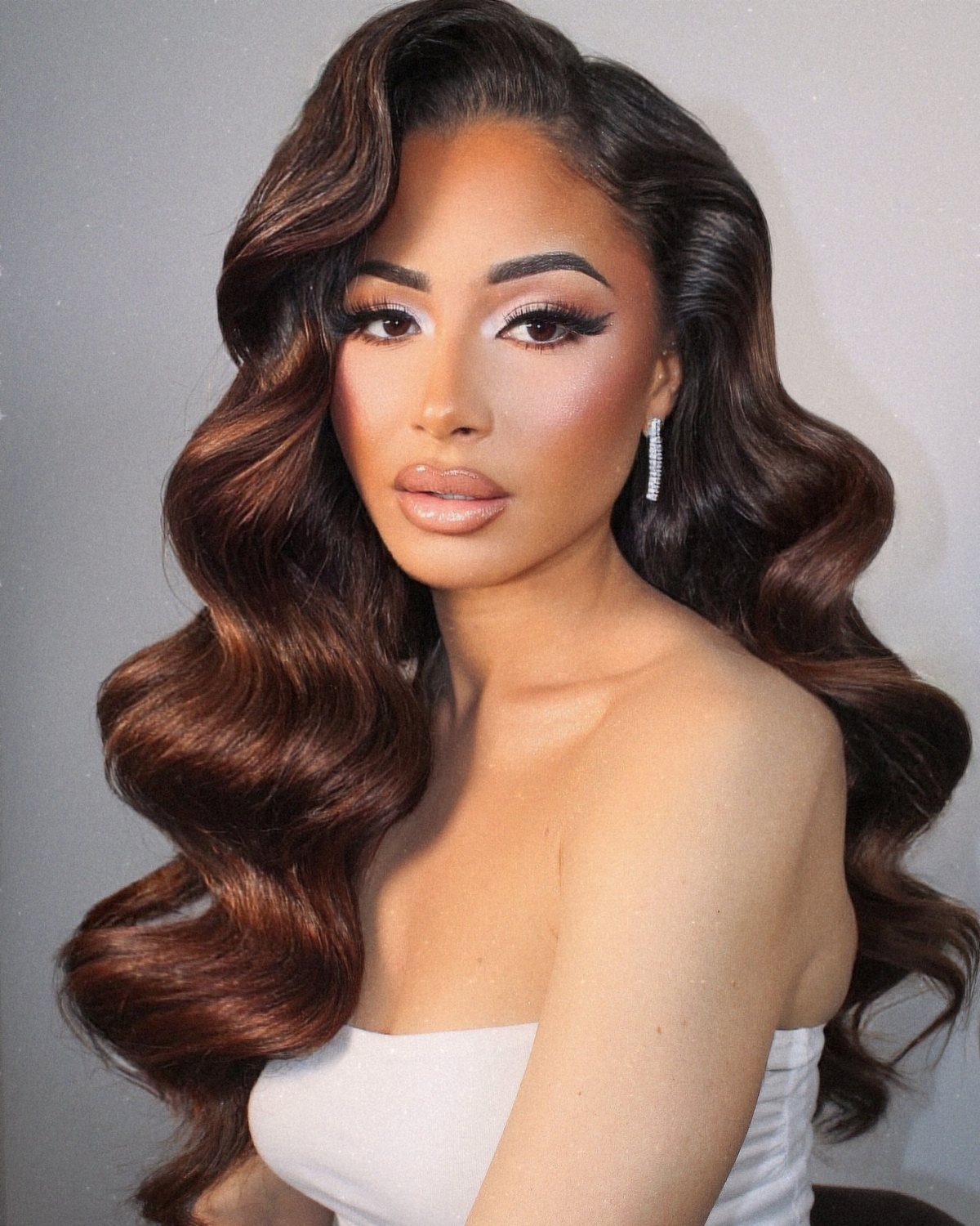 Woman with voluminous, glossy brown Hollywood waves and a white strapless top.