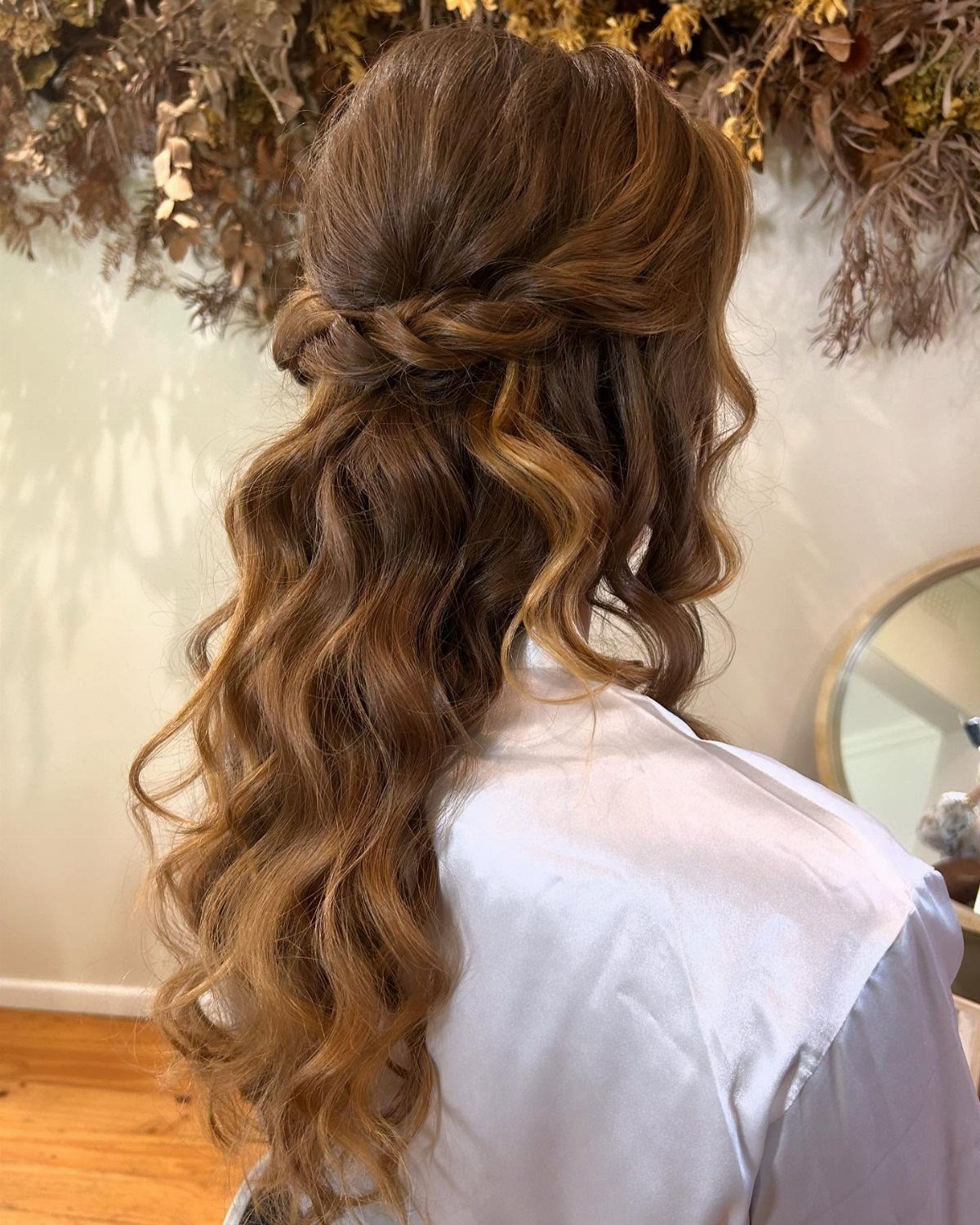 Wavy brown hair styled in a twisted half-up hairstyle with a white robe.