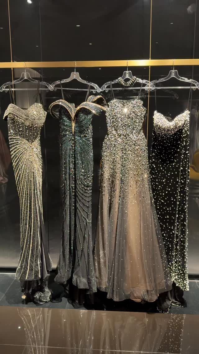 Four beaded and sequined evening gowns hanging on a gold clothing rack.