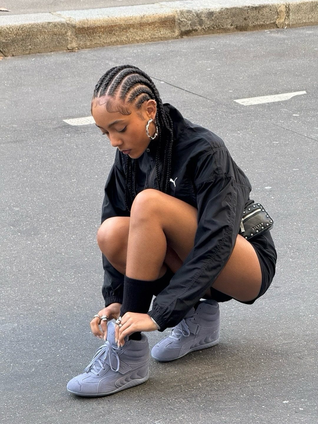 Woman in black athletic wear tying laces of grey hidden wedge sneakers outdoors.