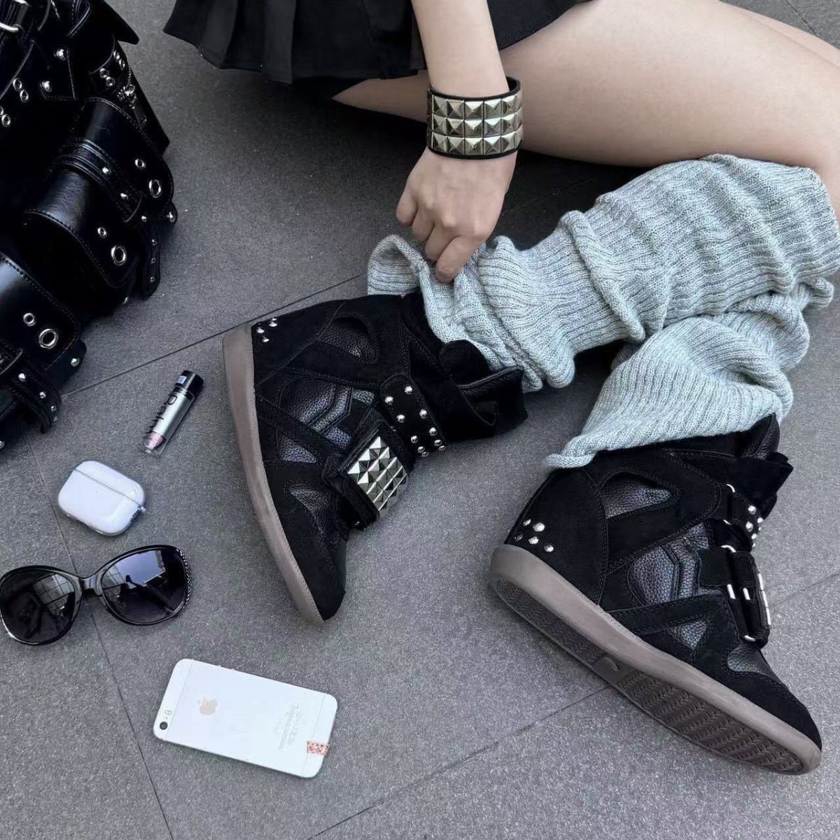 Black studded wedge sneakers worn with grey leg warmers on a grey floor