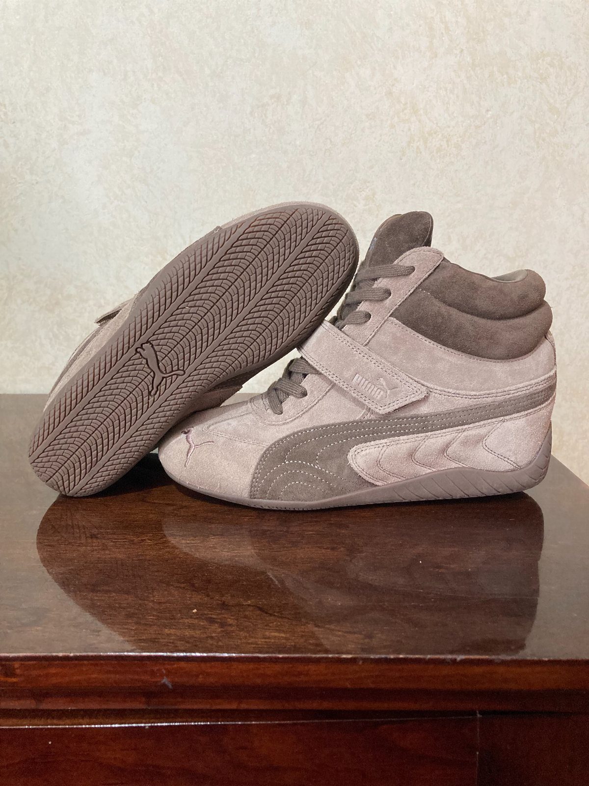 Taupe suede high-top sneakers with hidden wedges on a dark wooden table.