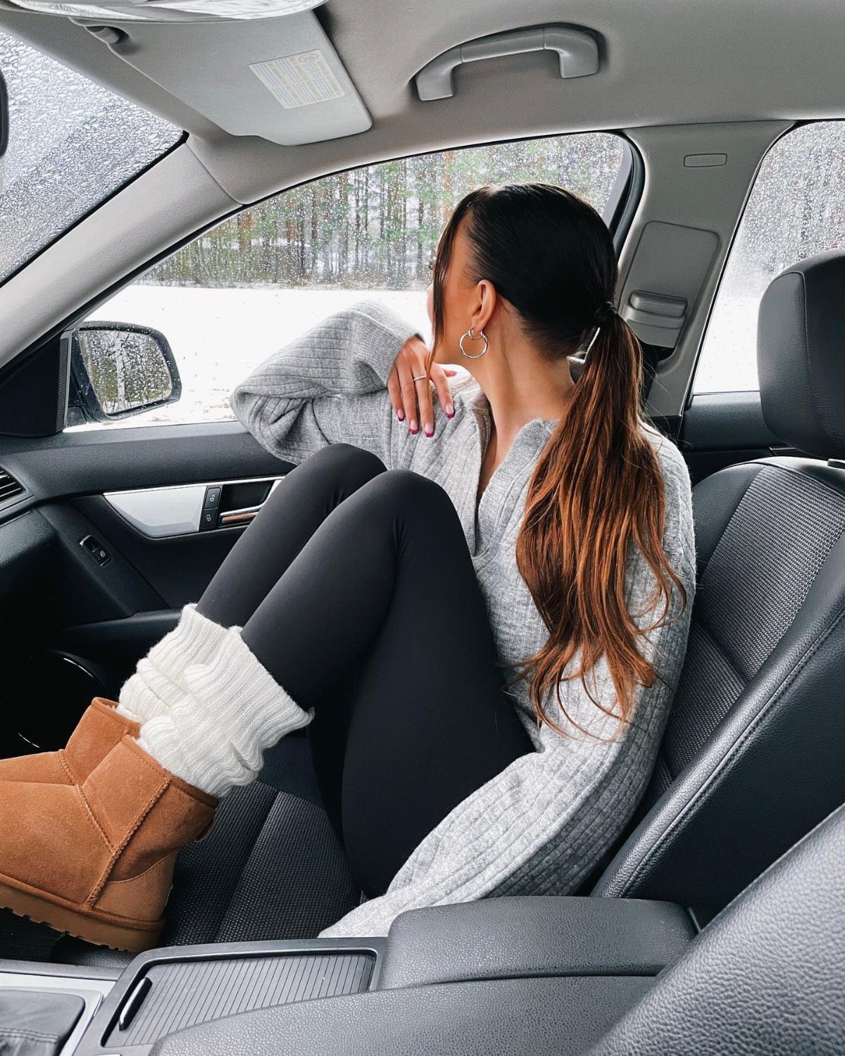 High UGG Boots: 6 Tall Styles From Classic to Adirondack 1 Woman in a car wearing a grey oversized sweater and tan UGG boots.