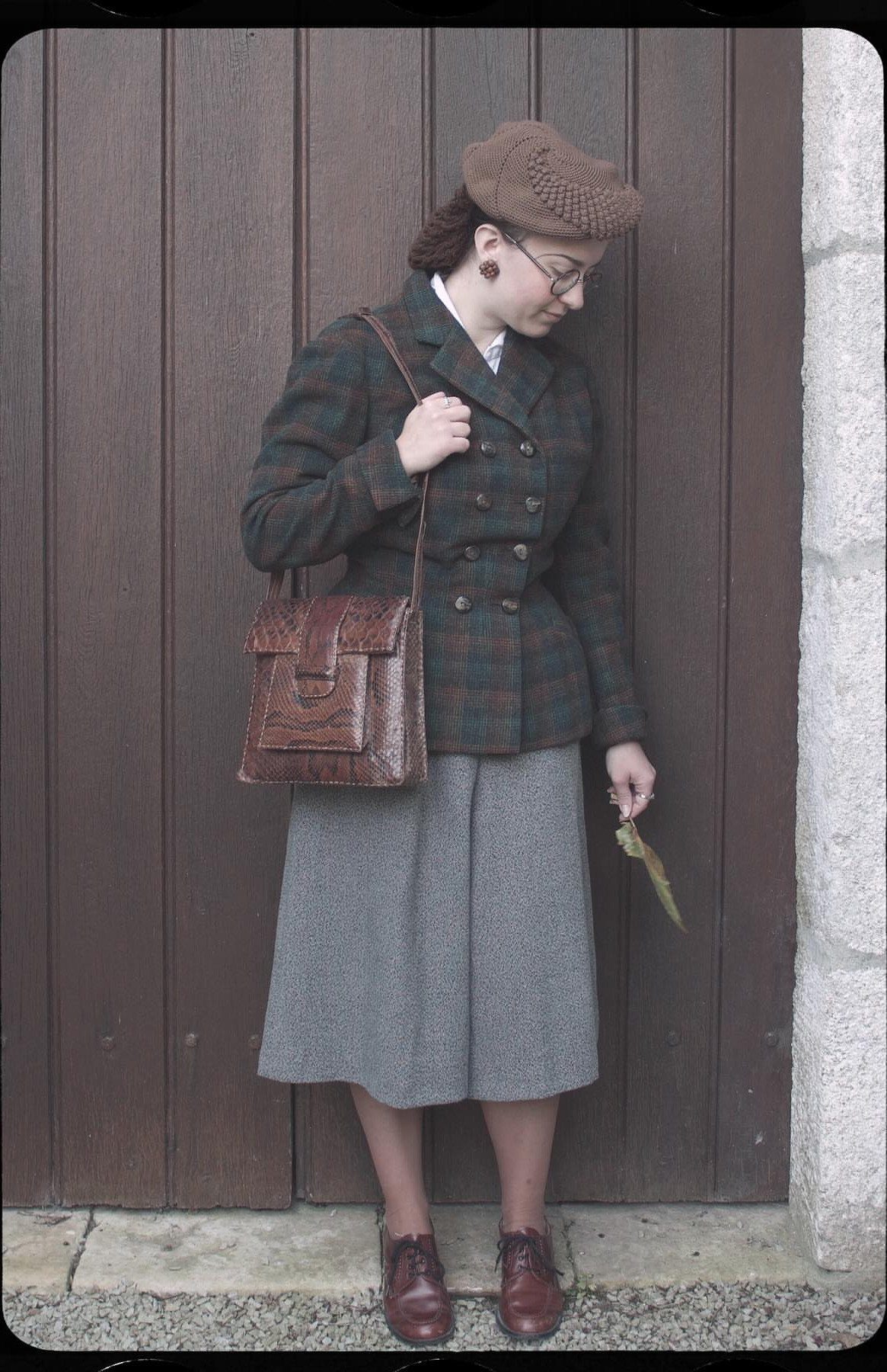 Woman in 1940s attire with plaid jacket, grey skirt, and brown beret.