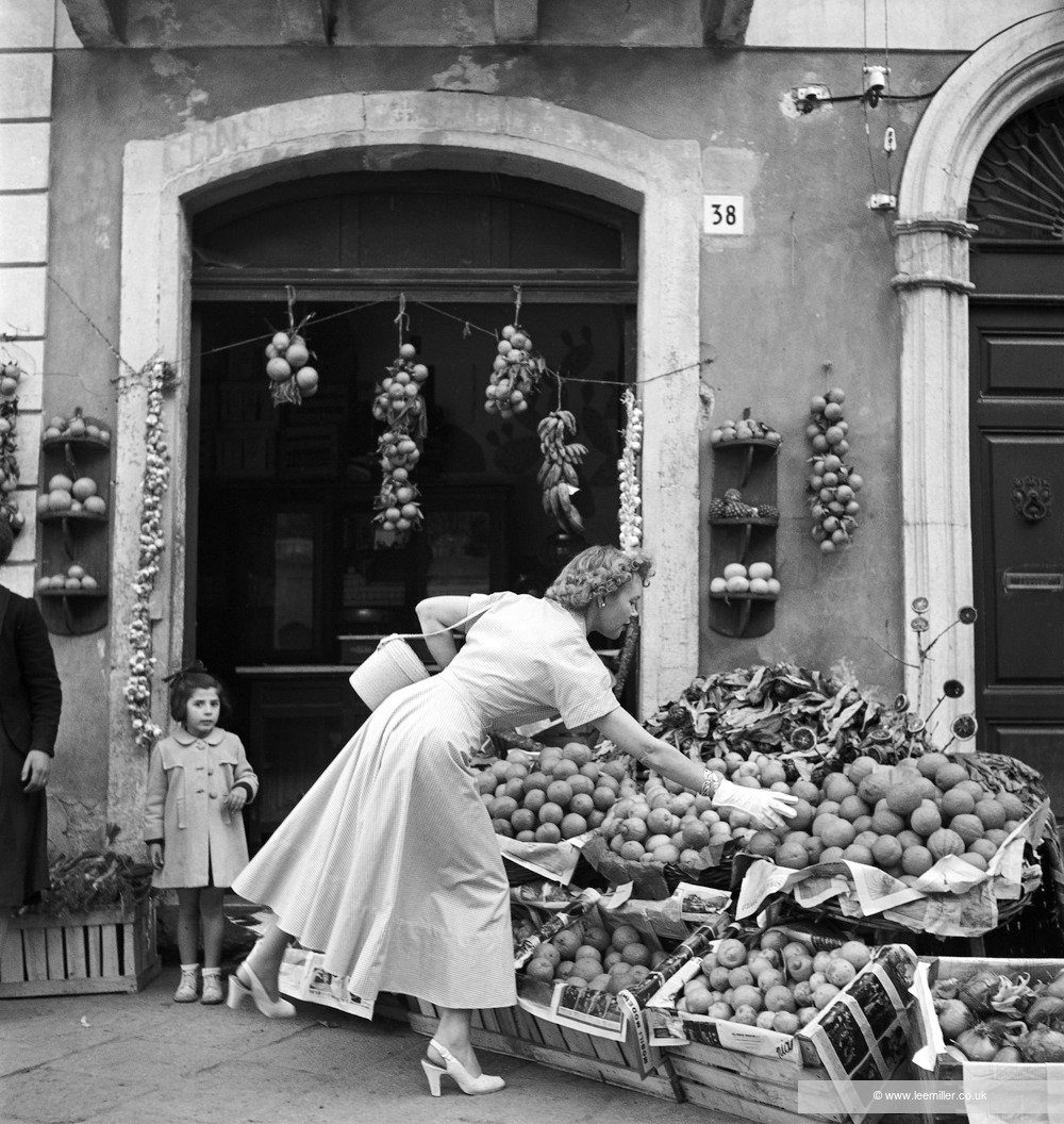 Woman in a flared mid-length dress shopping for produce at an outdoor market