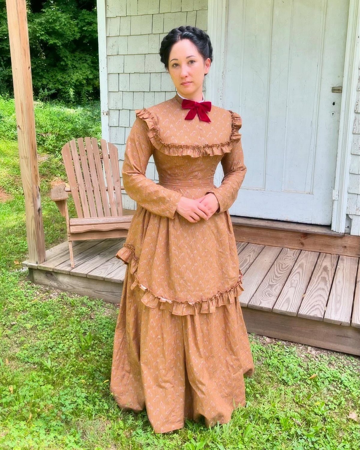 Woman in a brown striped Victorian dress with ruffles and a red bow.