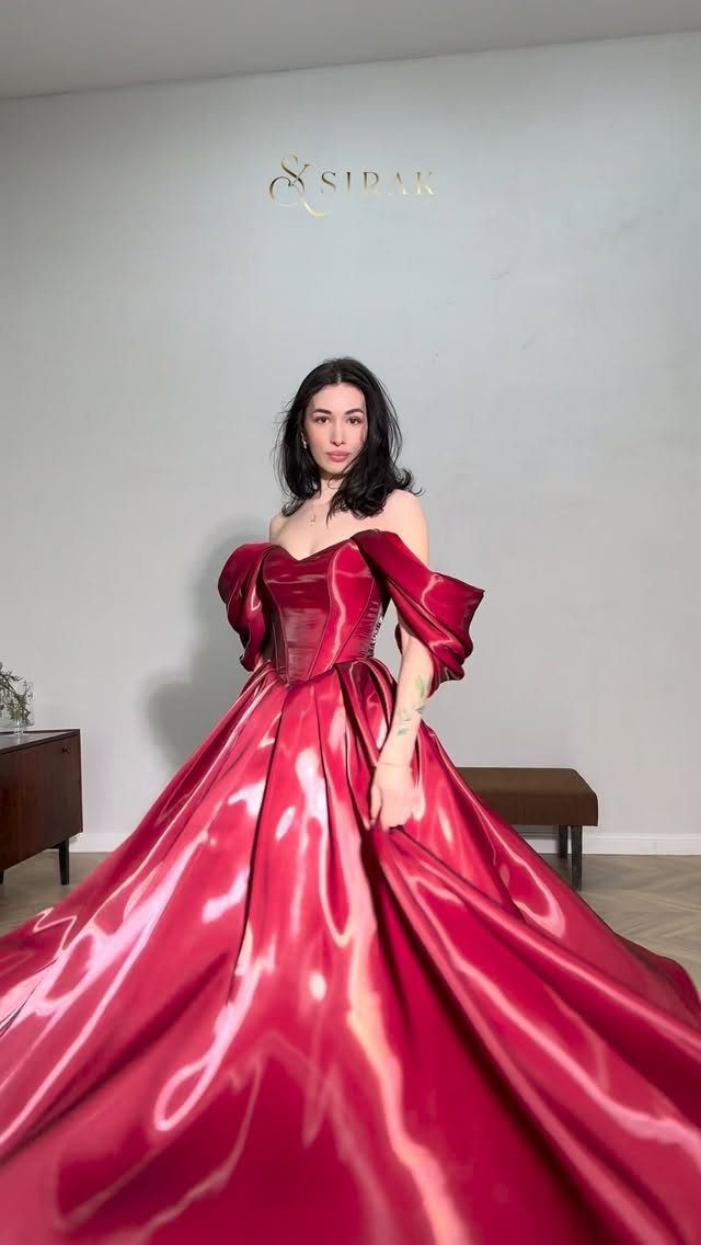 Woman wearing a voluminous shiny red satin off-the-shoulder ball gown in a room