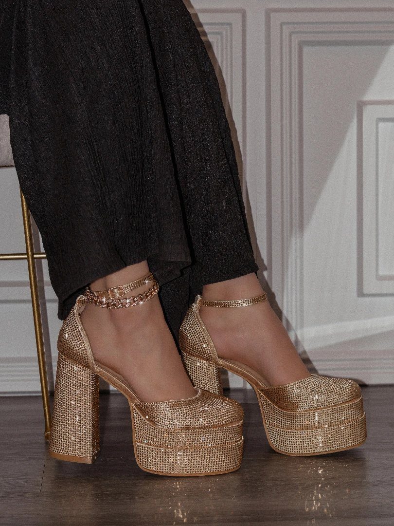 Gold glitter platform heels with chunky heels and ankle straps on a person.
