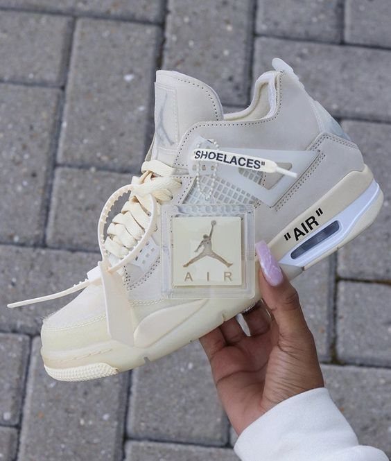 Cream and white Jordan sneaker held by a hand over grey stone pavement.