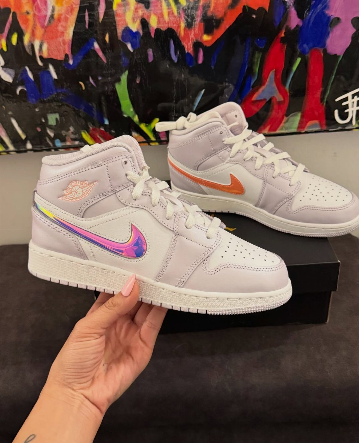 Light purple high-top sneakers with iridescent metallic swooshes held against abstract art.