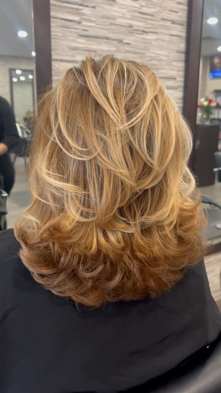Voluminous honey blonde layered blowout haircut with curled ends seen from behind.