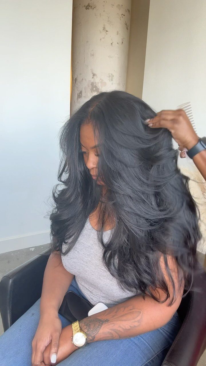 Woman with voluminous black layered blowout hair sitting in a salon chair.