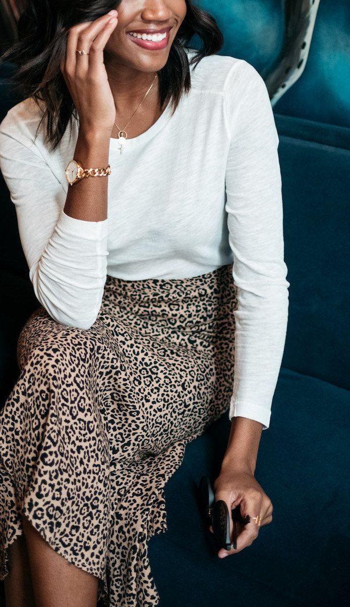 Woman in white top and leopard print midi skirt sitting on blue sofa