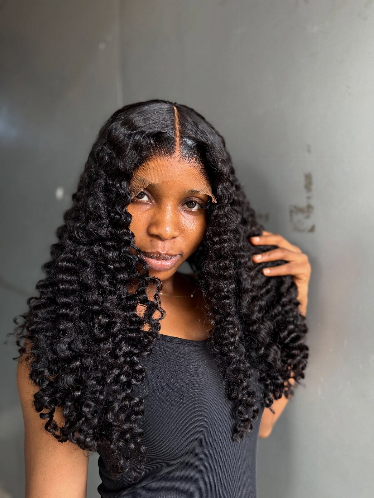 9 Long African Hair Ideas for Braids, Curls and Waves 1 Woman with long black curly hair and a middle part posing against grey wall